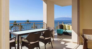 A balcony with a table and chairs, a sofa, and a view of the ocean.