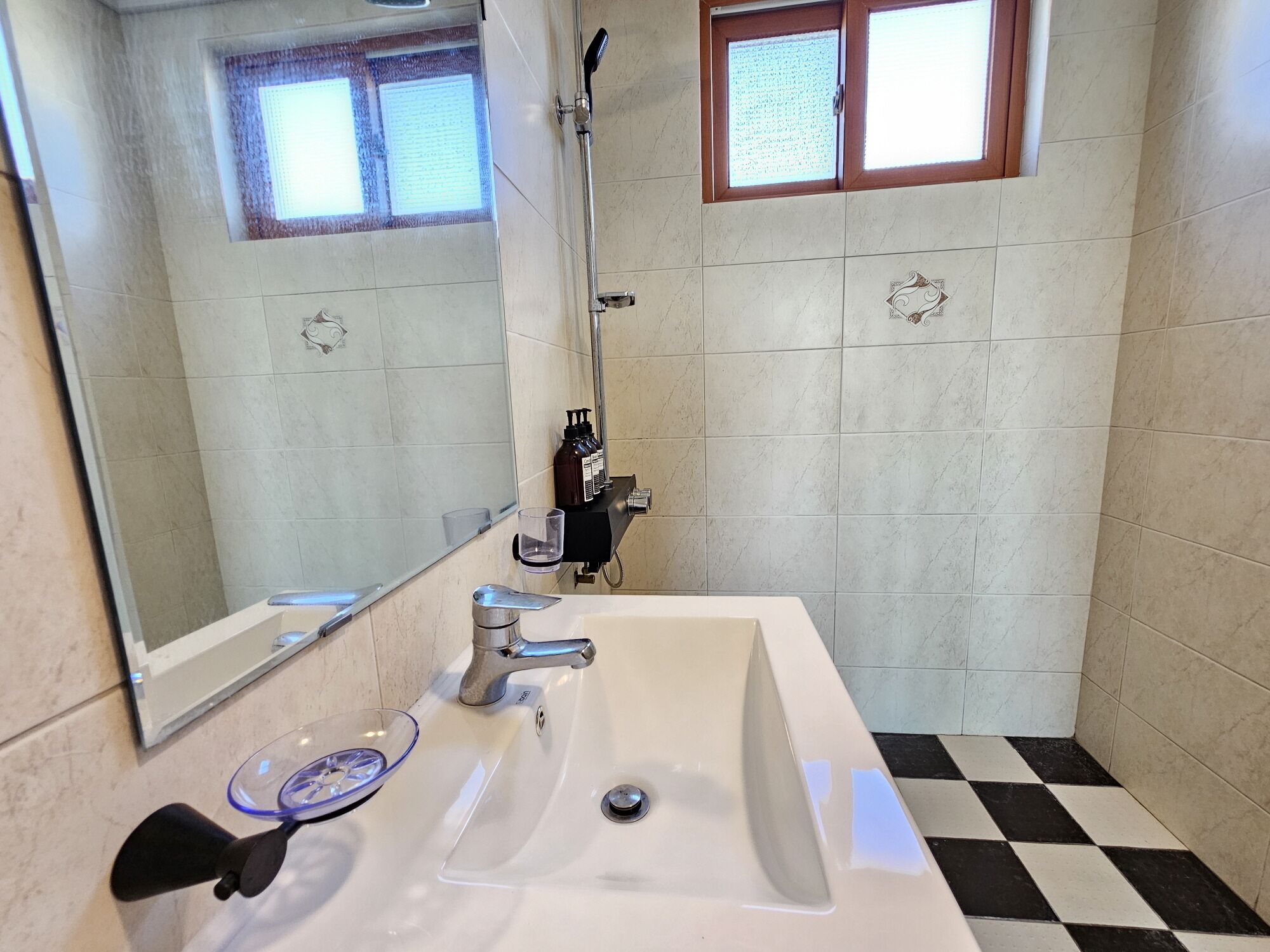 A bathroom with a large mirror, a sink, a shower, and a window.