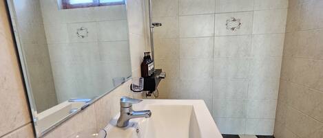 A bathroom with a large mirror, a sink, a shower, and a window.