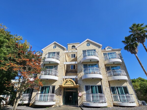 A multi-story hotel with a stone facade, multiple balconies, and a sign reading "Green Side." - Green Side Pension (Seogwipo)