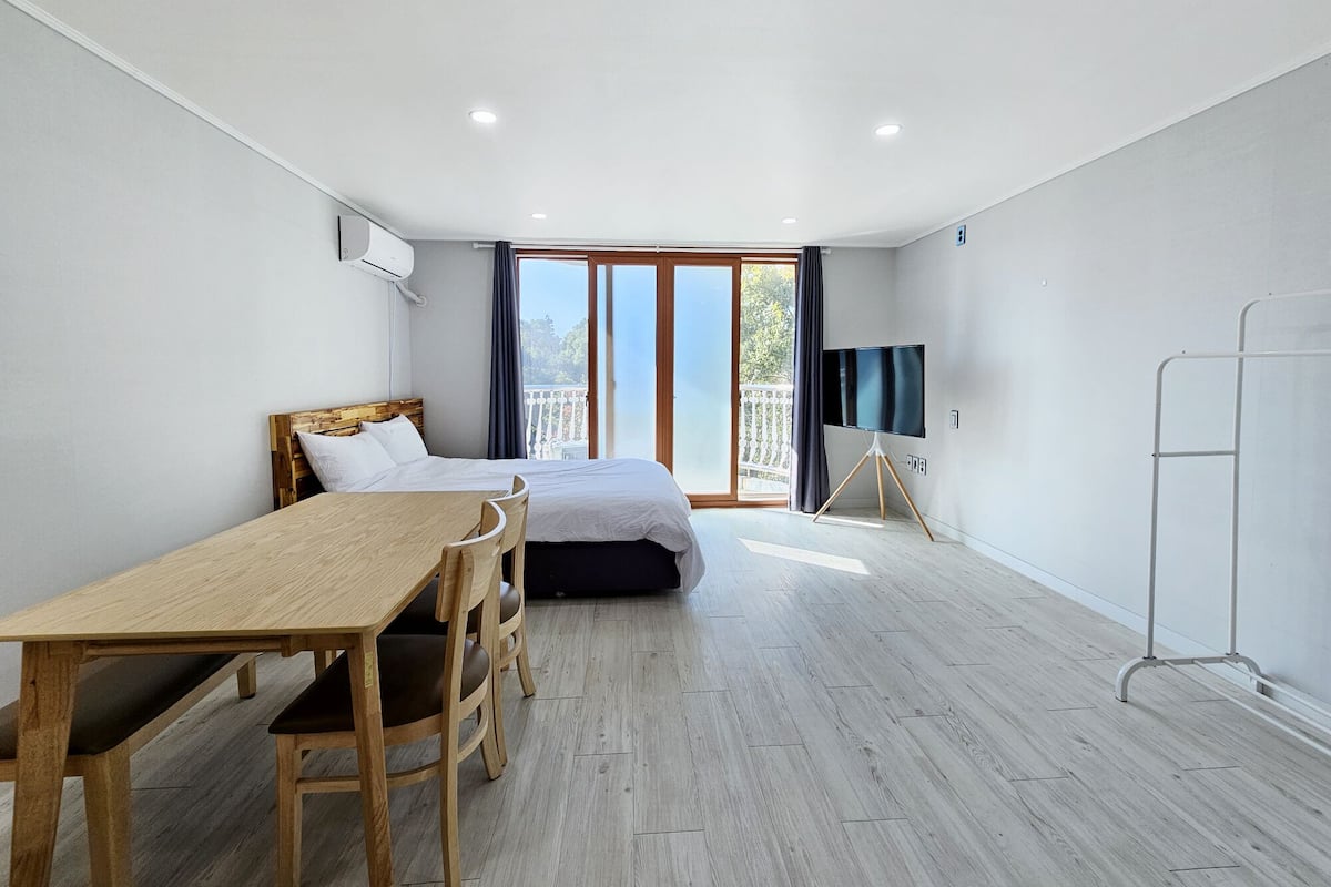 A modern bedroom with a wooden bed, a small desk, and a TV on a tripod stand.