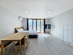 A modern bedroom with a wooden bed, a small desk, and a TV on a tripod stand. - Green Side Pension (Seogwipo)