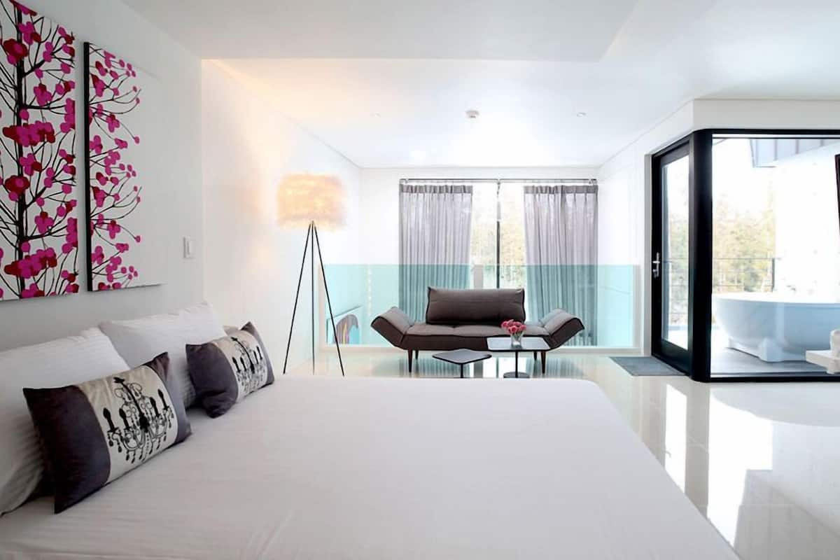 Una habitación de hotel moderna con una cama grande, un sofá, una mesita de vidrio y un televisor.