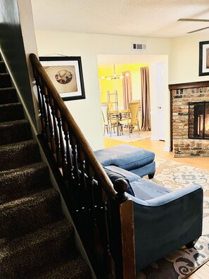 A staircase with wooden balusters leading to a living area with a blue sofa, a fireplace, and a dining area with yellow chairs. - LAVISH CONDO-BIG HOUSE MUSEUM, IDLE HR GOLF, WESLEYAN COLLEGE, MERCER UNIVERSITY (Macon)