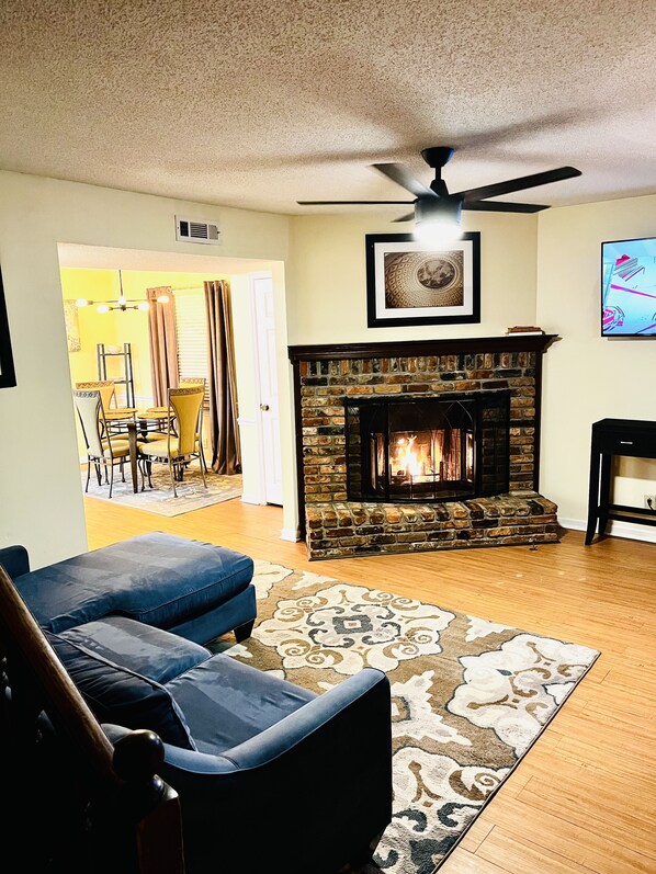 A living room with a stone fireplace, a ceiling fan, and a television. - LAVISH CONDO-BIG HOUSE MUSEUM, IDLE HR GOLF, WESLEYAN COLLEGE, MERCER UNIVERSITY (Macon)