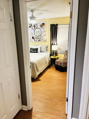 A bedroom with a bed, a bedside table, a lamp, a chair, and a wall art piece. - LAVISH CONDO-BIG HOUSE MUSEUM, IDLE HR GOLF, WESLEYAN COLLEGE, MERCER UNIVERSITY (Macon)