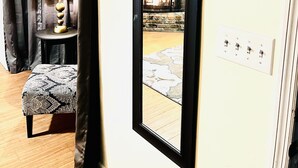 A room with a large mirror, a lamp, a patterned ottoman, a fireplace, and a power outlet.