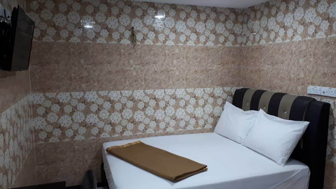 A hotel room with a bed, a brown blanket, and patterned wallpaper.