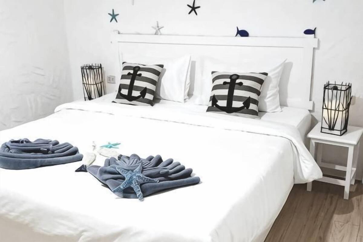 Ein ordentlich gemachstes Bett mit gestreiften Kissen, einer Meerstern-Dekoration und gefalteten Handtüchern auf einer weißen Bettdecke.