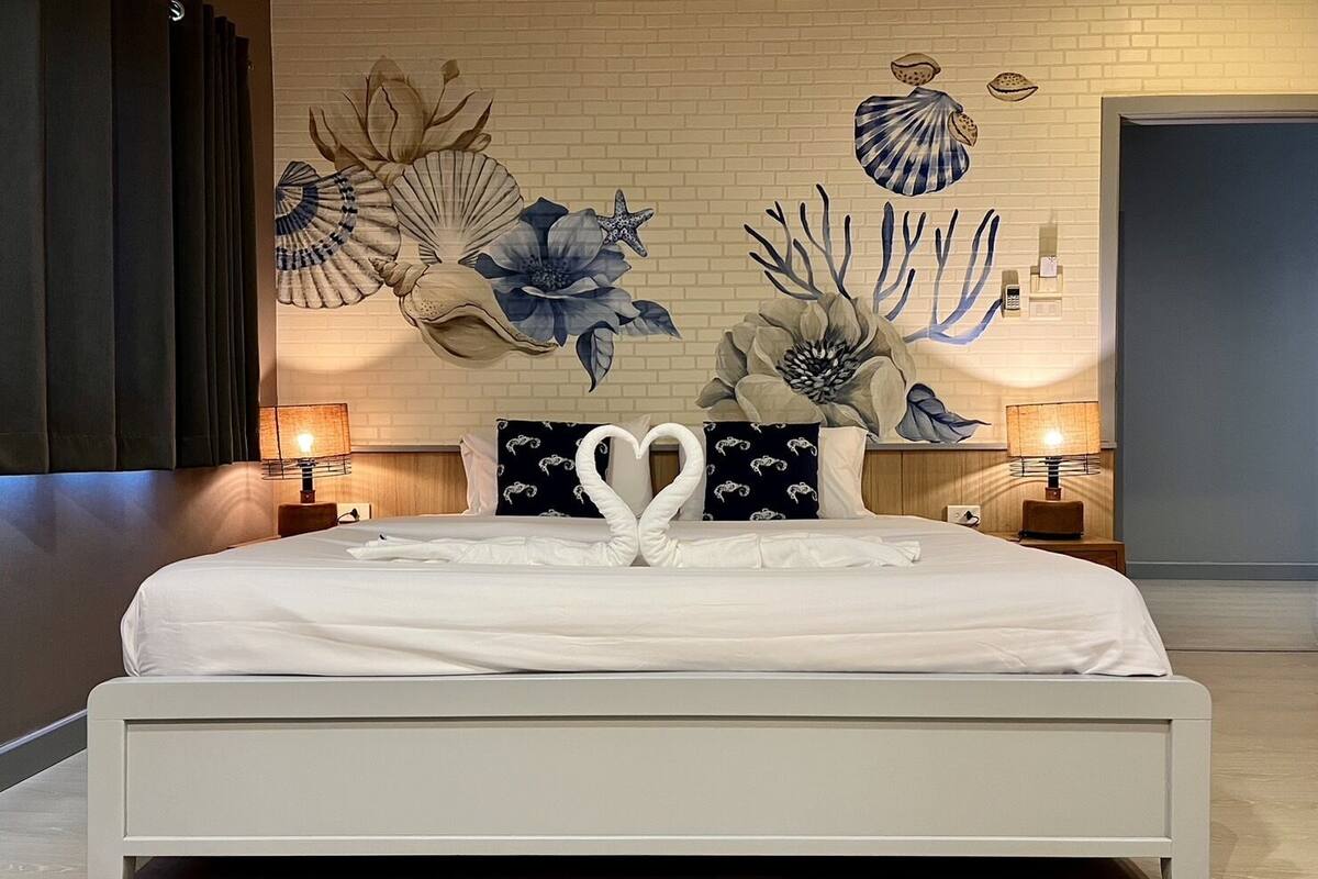 Ein Schlafzimmer mit einem großen Bett, zwei Nachttischen mit Lampen und einem Wandgemälde von Meereslebewesen.