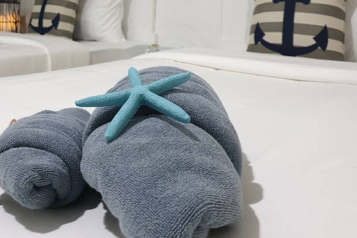 Ein ordentlich bezogenes Bett mit einem Seestern-Dekor, gestreiften Kissen und einer Wanddekoration im maritimen Stil.