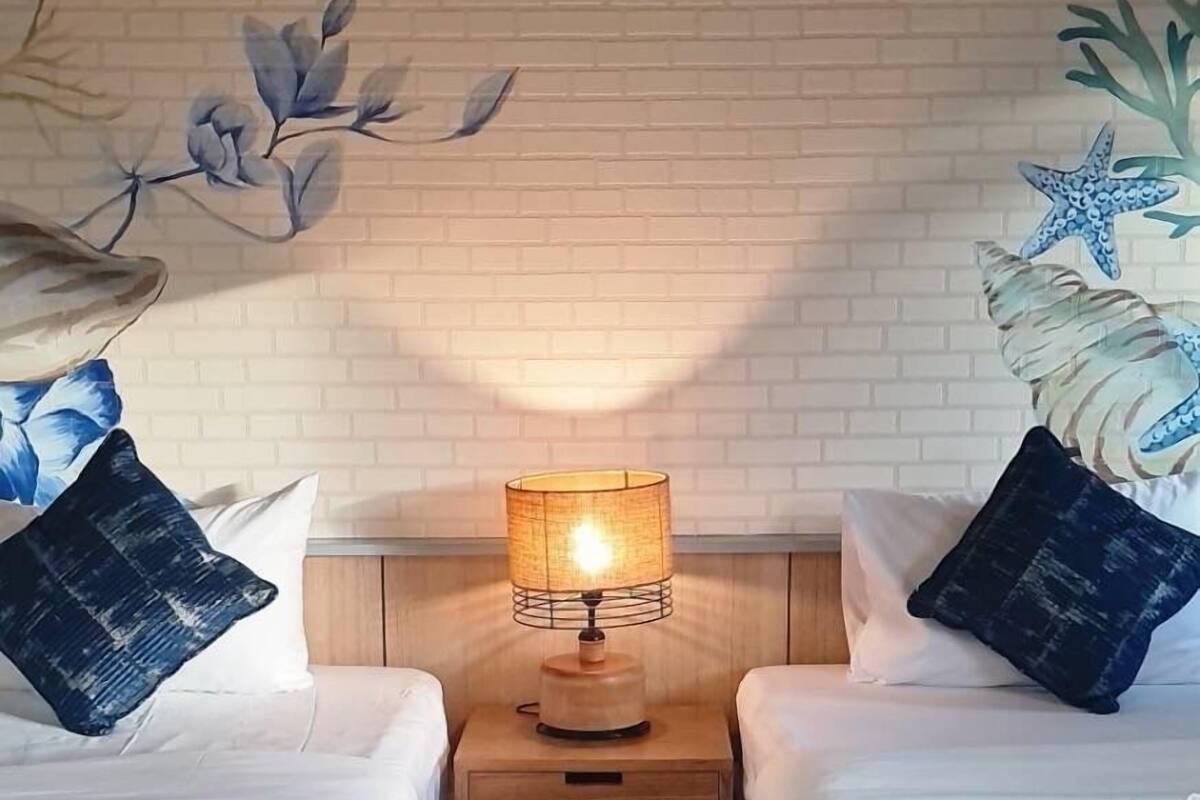 Ein Hotelzimmer mit zwei Betten, einem Nachttisch mit Lampe und einem Wandgemälde.
