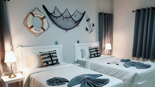 Habitación de hotel con dos camas, cada una con un cojín que presenta un diseño de ancla, un flotador y una red en la pared.