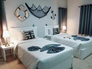 Ein Hotelzimmer mit zwei Betten, jedes mit einem Kissen mit Anker-Motiv, einem Rettungsring und einem Netz an der Wand.