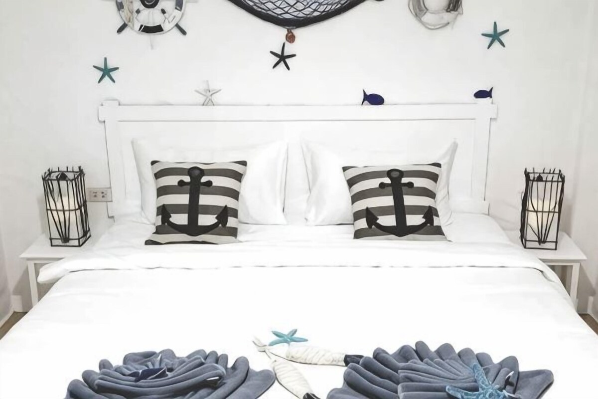 Una cama con ropa de cama blanca, dos almohadas con diseños de anclas y una mosquitera colgada encima.