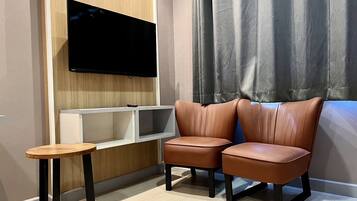A modern living room with a mounted TV, two leather chairs, a small wooden table, and a white shelving unit.