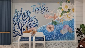 Pared con un mural de arrecife de coral y flores, dos sillas blancas y una lámpara de techo.