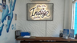 Un mostrador de recepción con un cartel que dice 'Welcome', un letrero en la pared del hotel 'Phi Phi Indige' y una decoración con un ancla náutica.