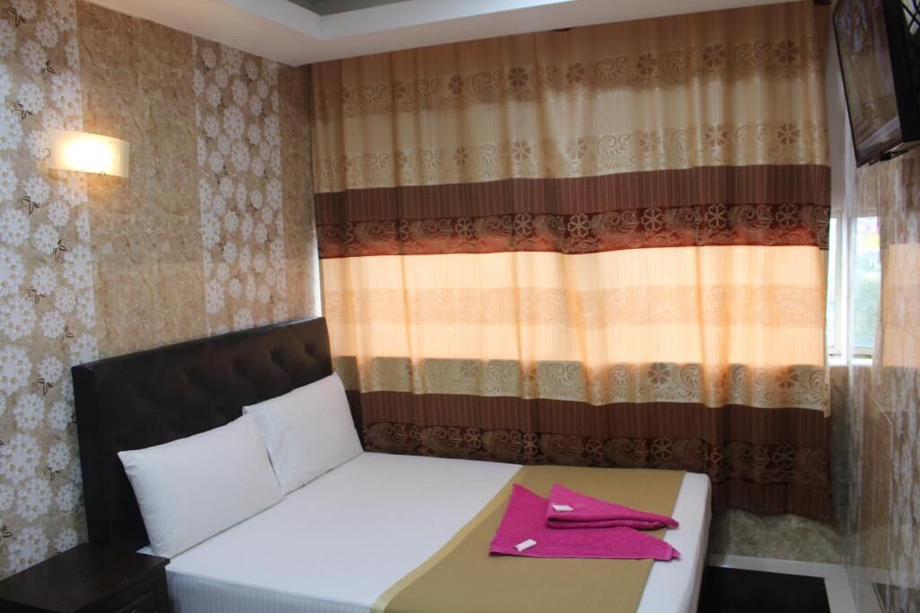 Una habitación de hotel con una cama, una mesita de noche y un ventanal con cortinas.