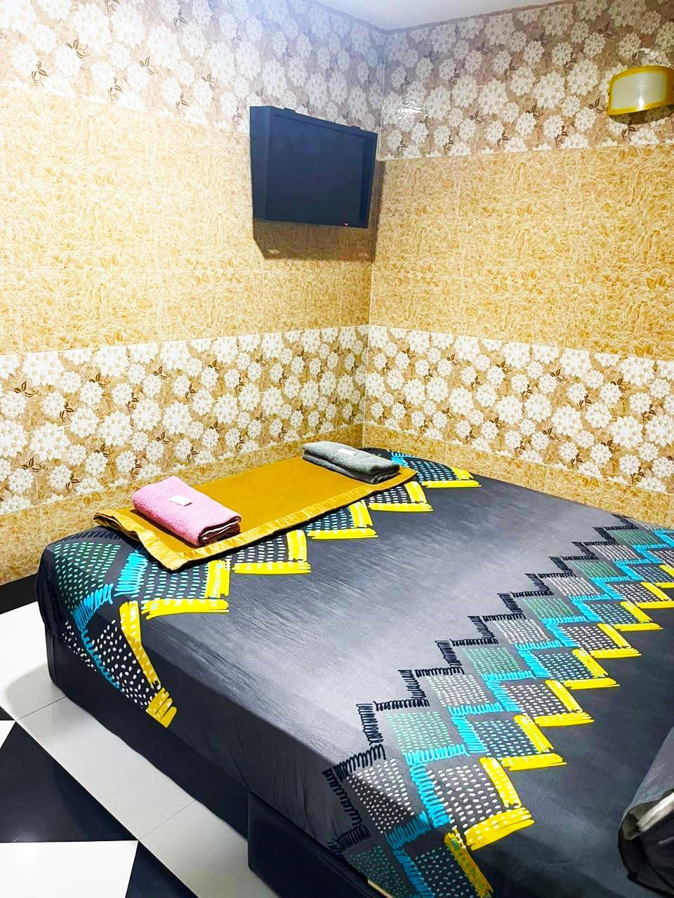 Una habitación con una cama, un televisor montado en la pared y un papel tapiz estampado.