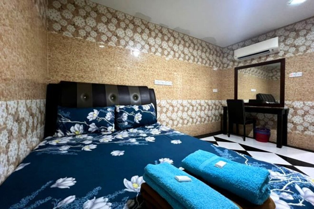 A hotel room with a bed, a desk, and an air conditioning unit.