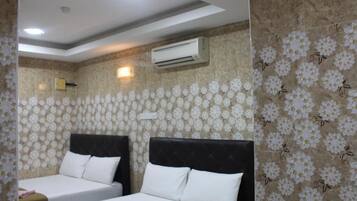 A hotel room with two beds, floral wallpaper, an air conditioning unit, and a ceiling light.