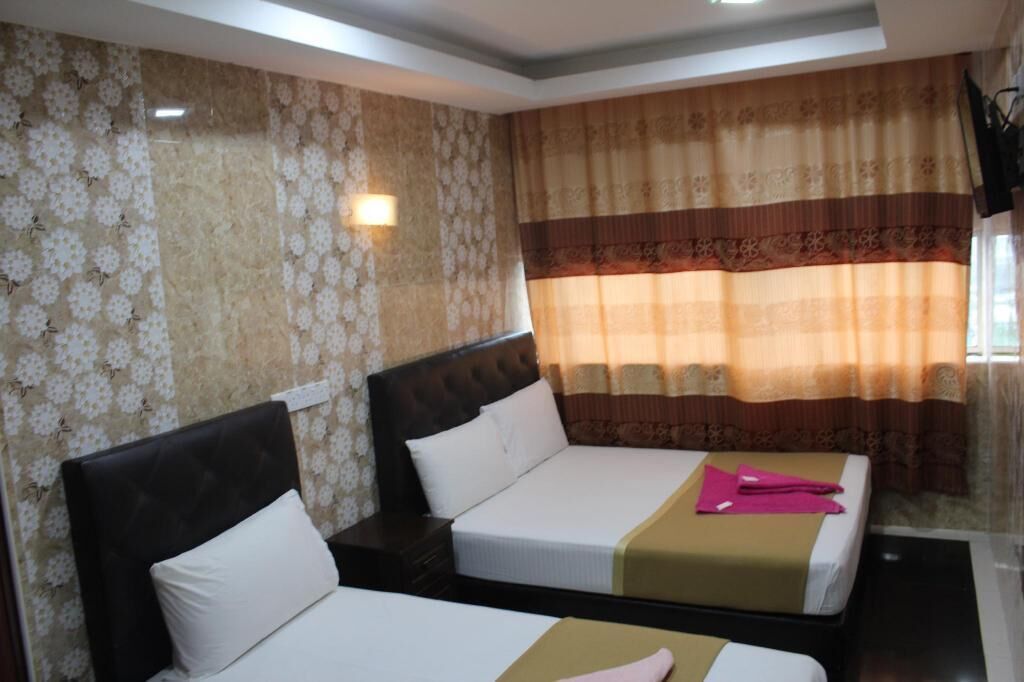A hotel room with two beds, floral wallpaper, a headboard, and a window with curtains.