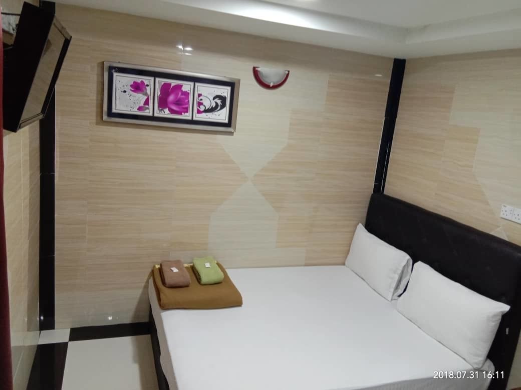Habitación de hotel con cama, una mesita con un cojín marrón y verde, y un marco de fotos en la pared.