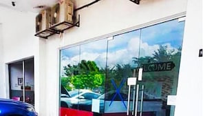 Entrada de un edificio moderno con puerta de vidrio, alfombra roja y un coche azul estacionado afuera.