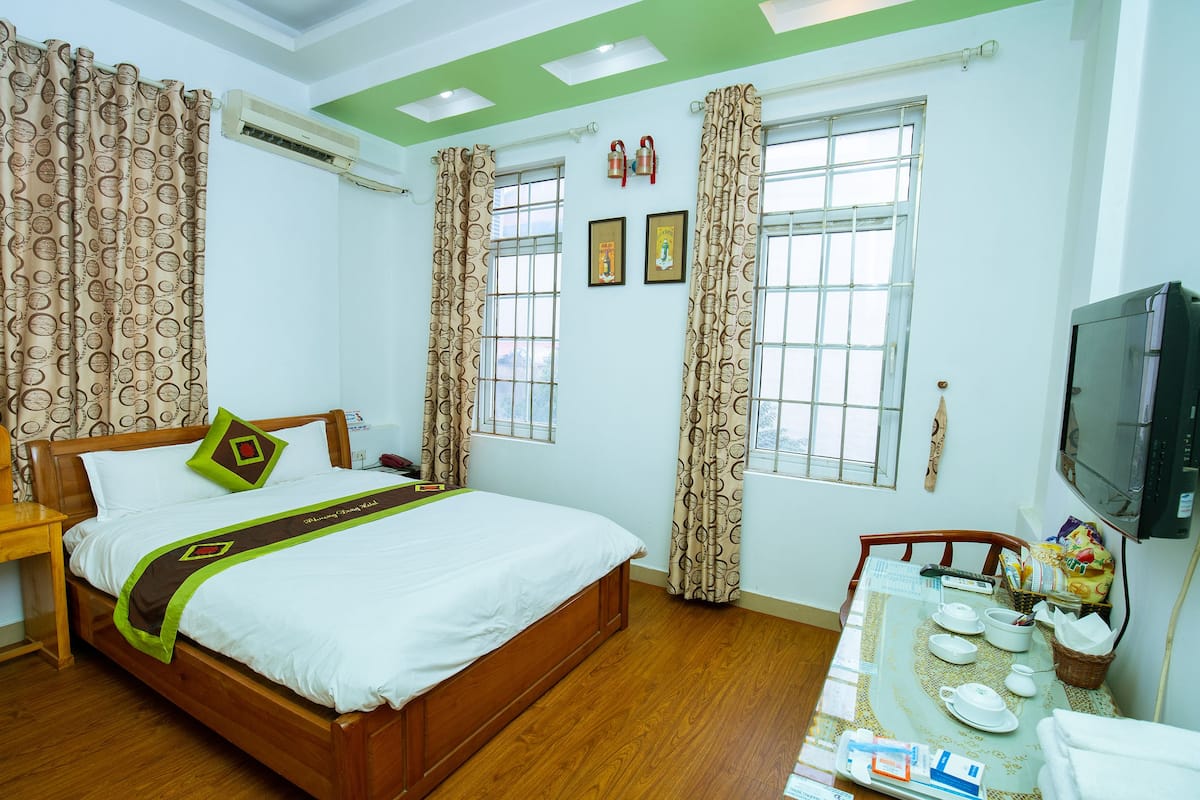 A hotel room with a wooden bed, a desk, a television, and a dining table set for breakfast.