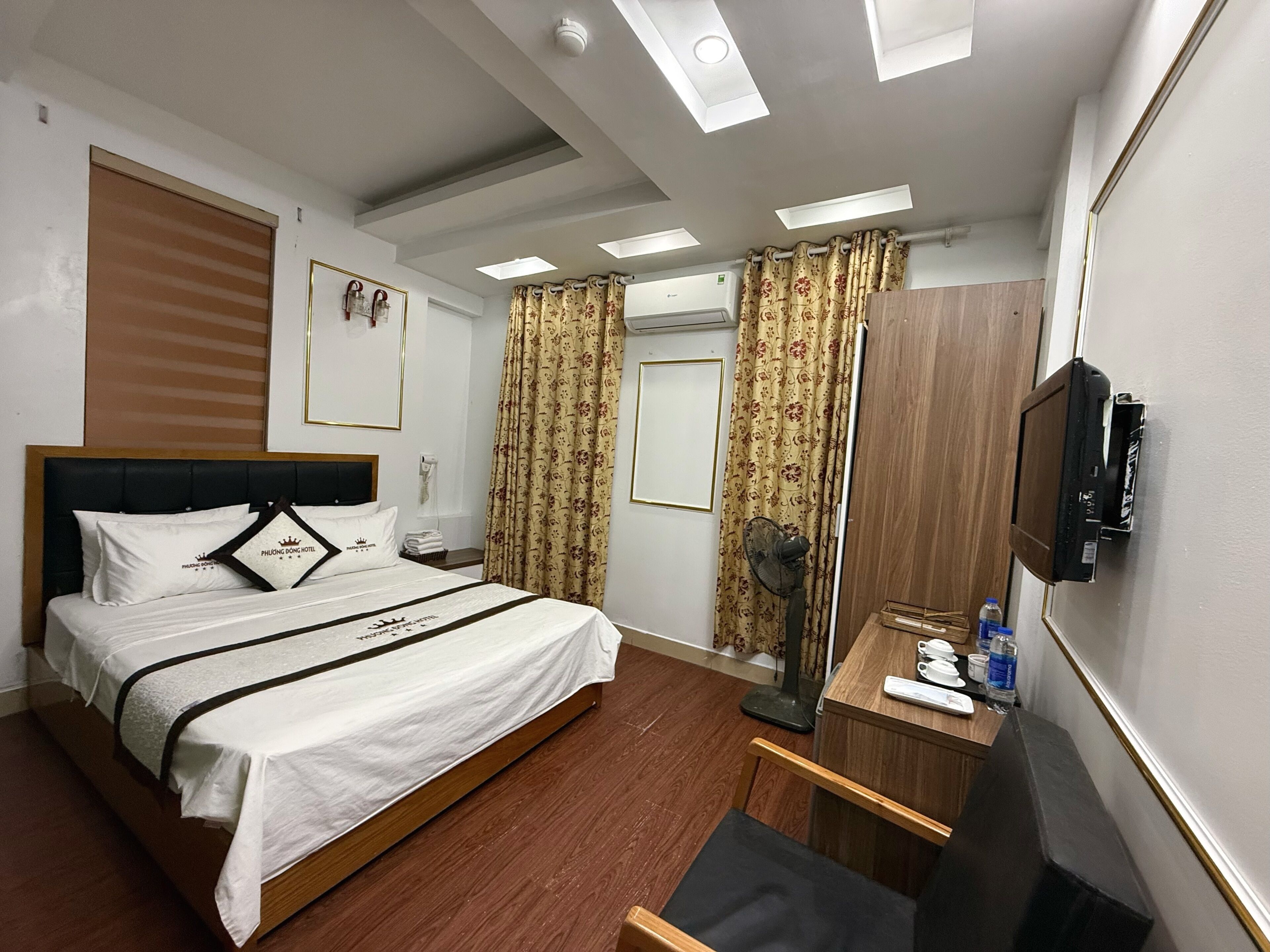 A hotel room with a bed, bedside table, TV, and a desk with a chair.