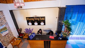 A hotel reception desk with a clock, a sign indicating the hotel name, and a plant.