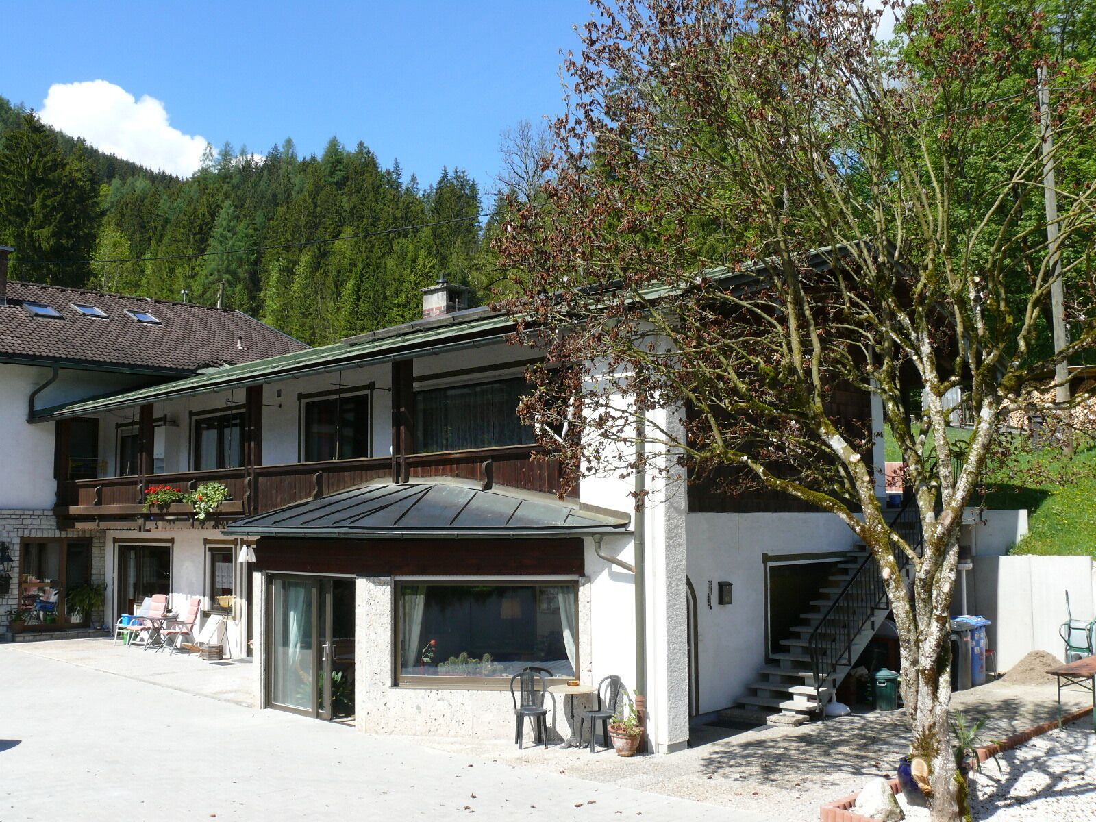Ein zweistöckiges Gebäude mit Balkon, überdachter Terrasse und einer Treppe, die zu einer oberen Etage führt.