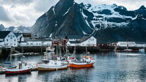 A harbor with boats docked, a mountain in the background, and buildings along the waterfront. - Lofoten Apartments (Vagan)