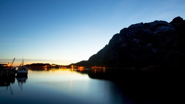 A calm harbor at dusk with boats docked, a mountain in the background, and a clear sky. - Lofoten Apartments (Vagan)