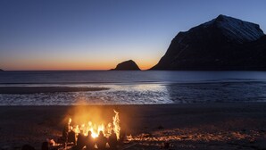 A beach scene with a campfire and a mountain in the background. - Lofoten Apartments (Vagan)
