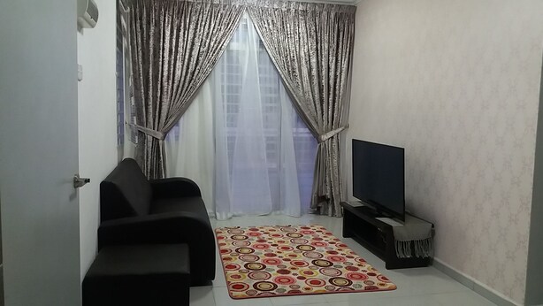 A living room with a black sofa, a TV on a stand, a patterned rug, and sheer curtains. - Kasa Heights Homestay (Alor Gajah)