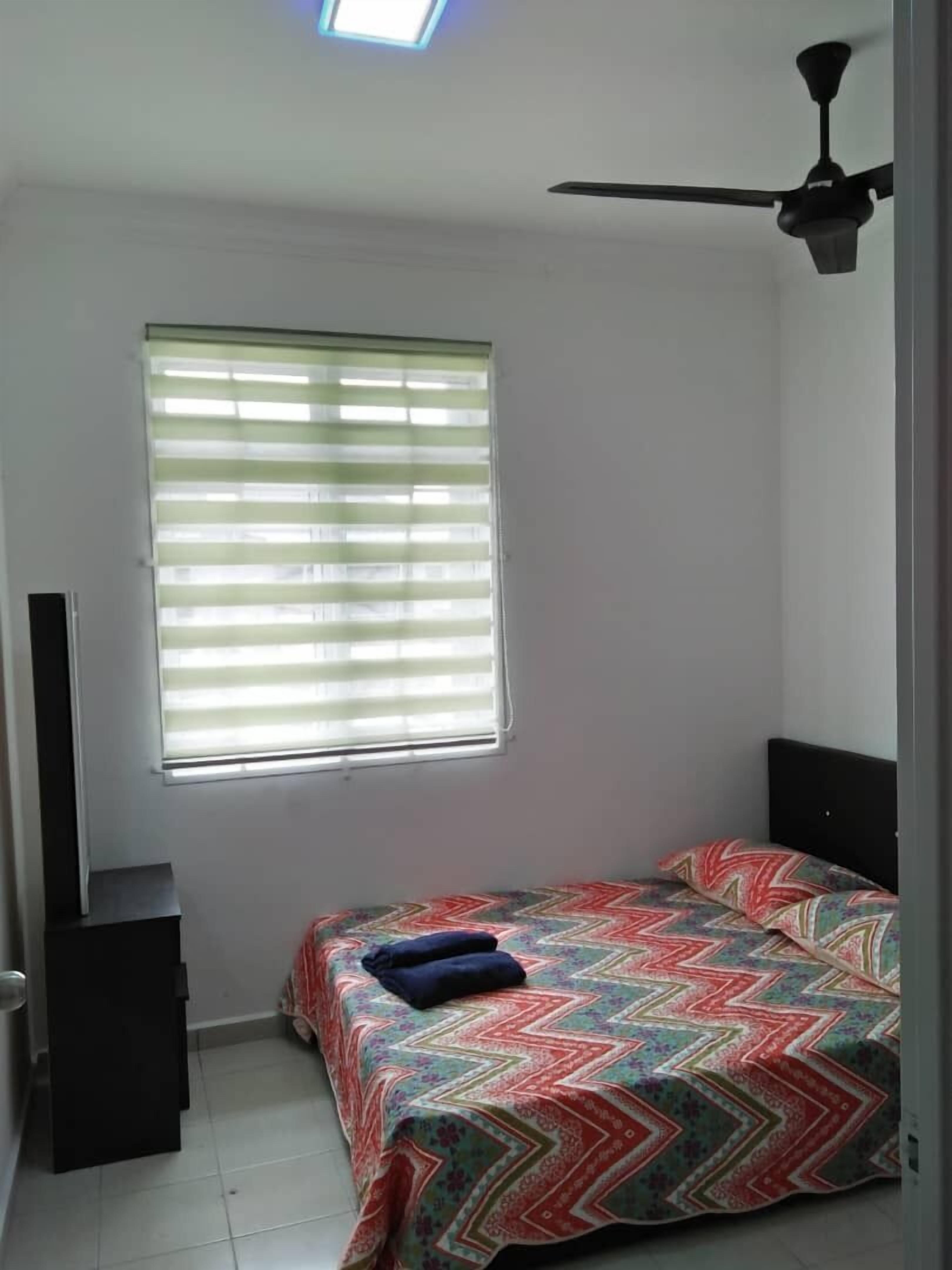 A bedroom with a bed, a ceiling fan, a window with blinds, and a small black cabinet.