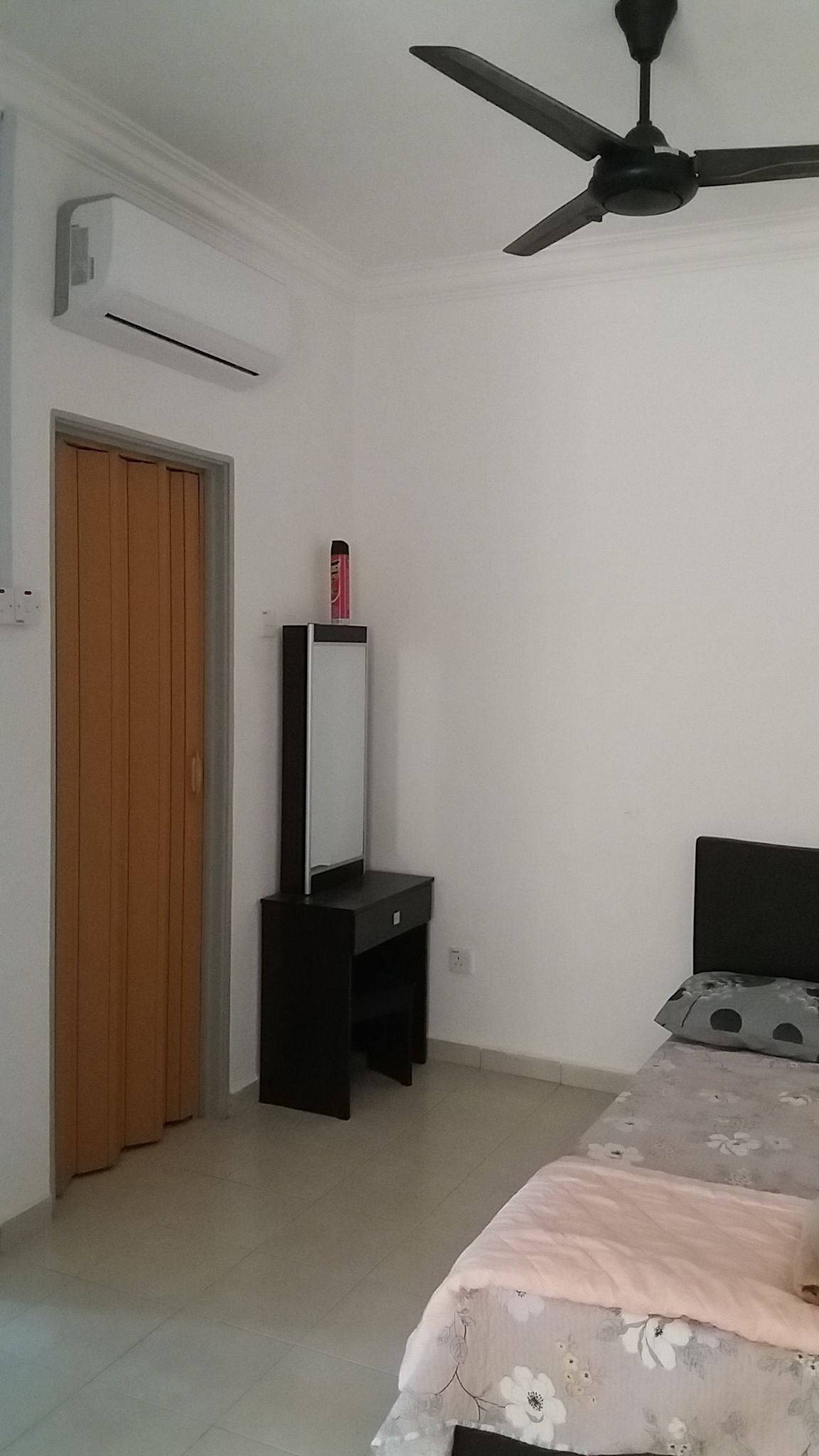 A bedroom with a bed, a wardrobe, a desk with a mirror, and a ceiling fan.
