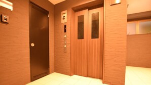 An elevator with a control panel, wooden doors, and a tiled floor. - MT House Bentencho (Osaka)