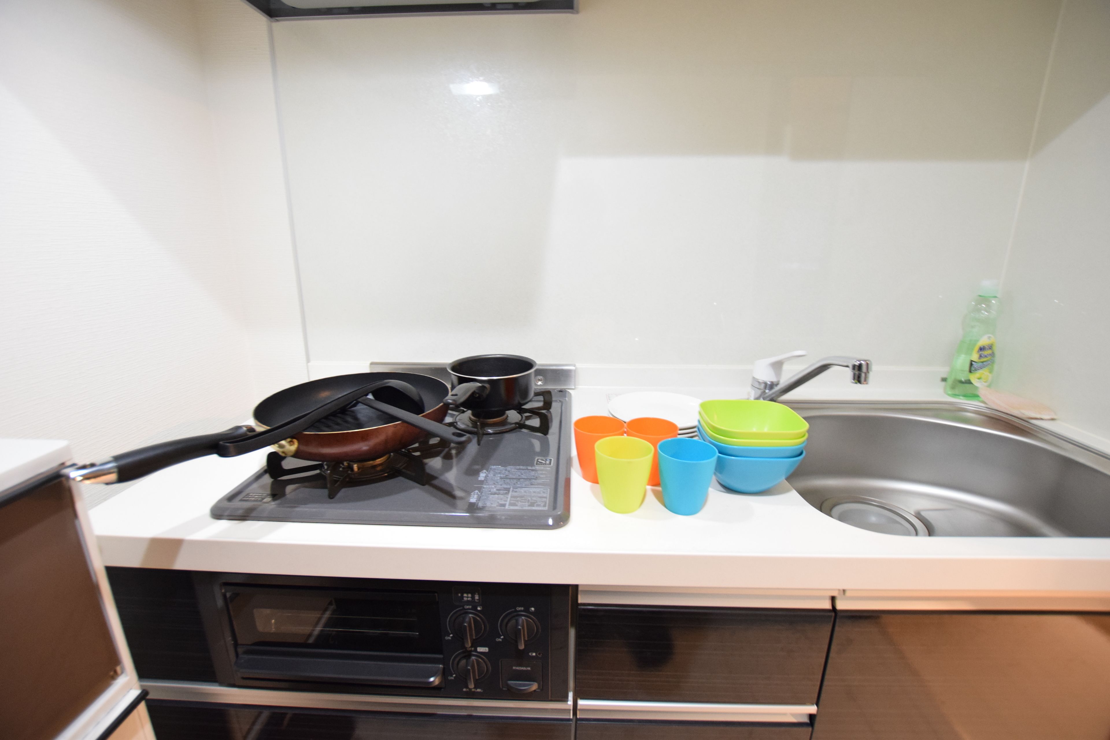 A kitchen with a stove, pots, a sink, and colorful cups.