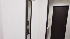 A hallway with a dark wooden door, a white wall, and a framed artwork above the door. - MT House Bentencho (Osaka)