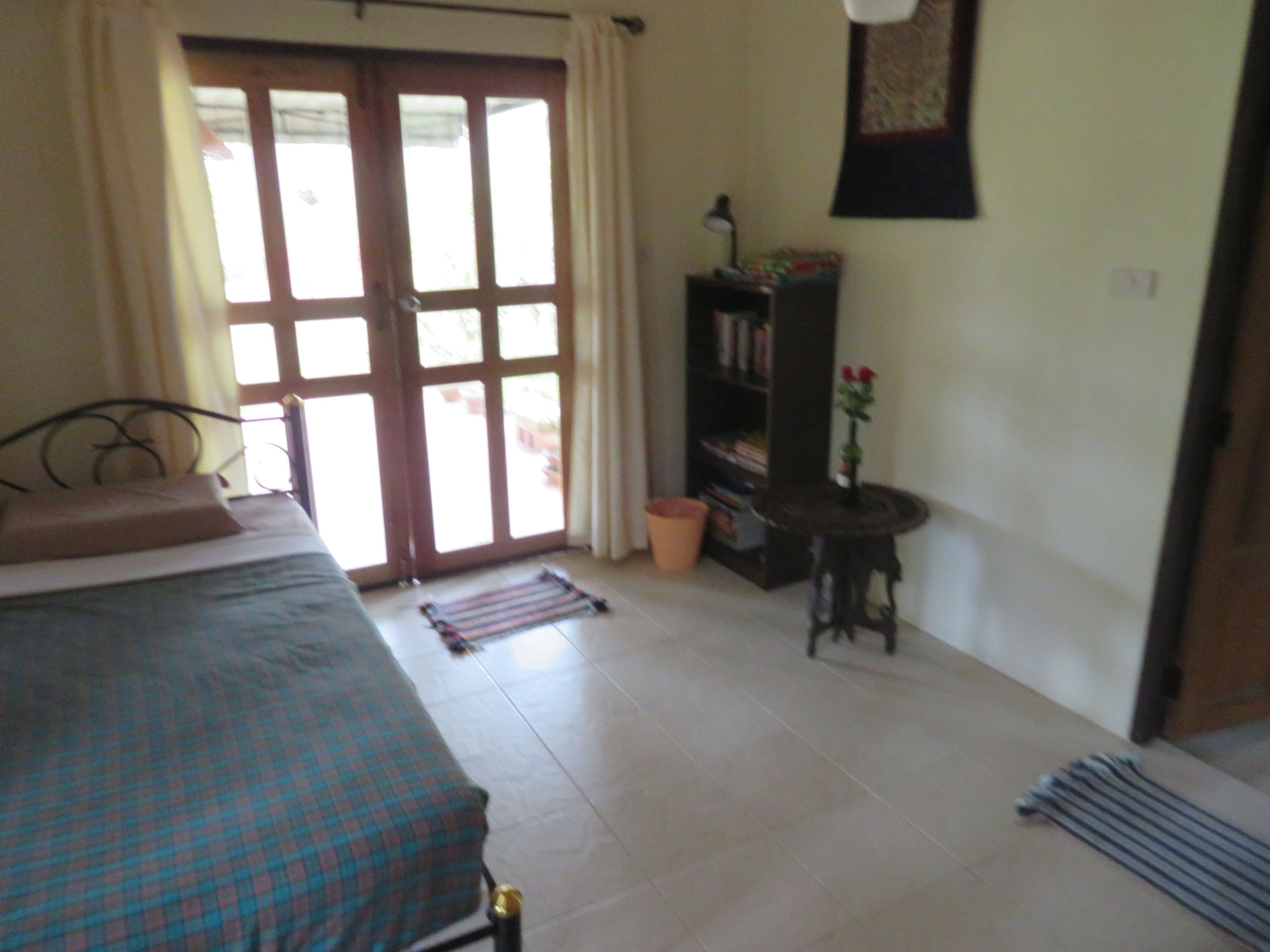 A bedroom with a bed, a bookshelf, a small table, and a window with curtains.