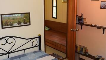Quarto com cama, porta de madeira, estante com livros e quadros nas paredes.