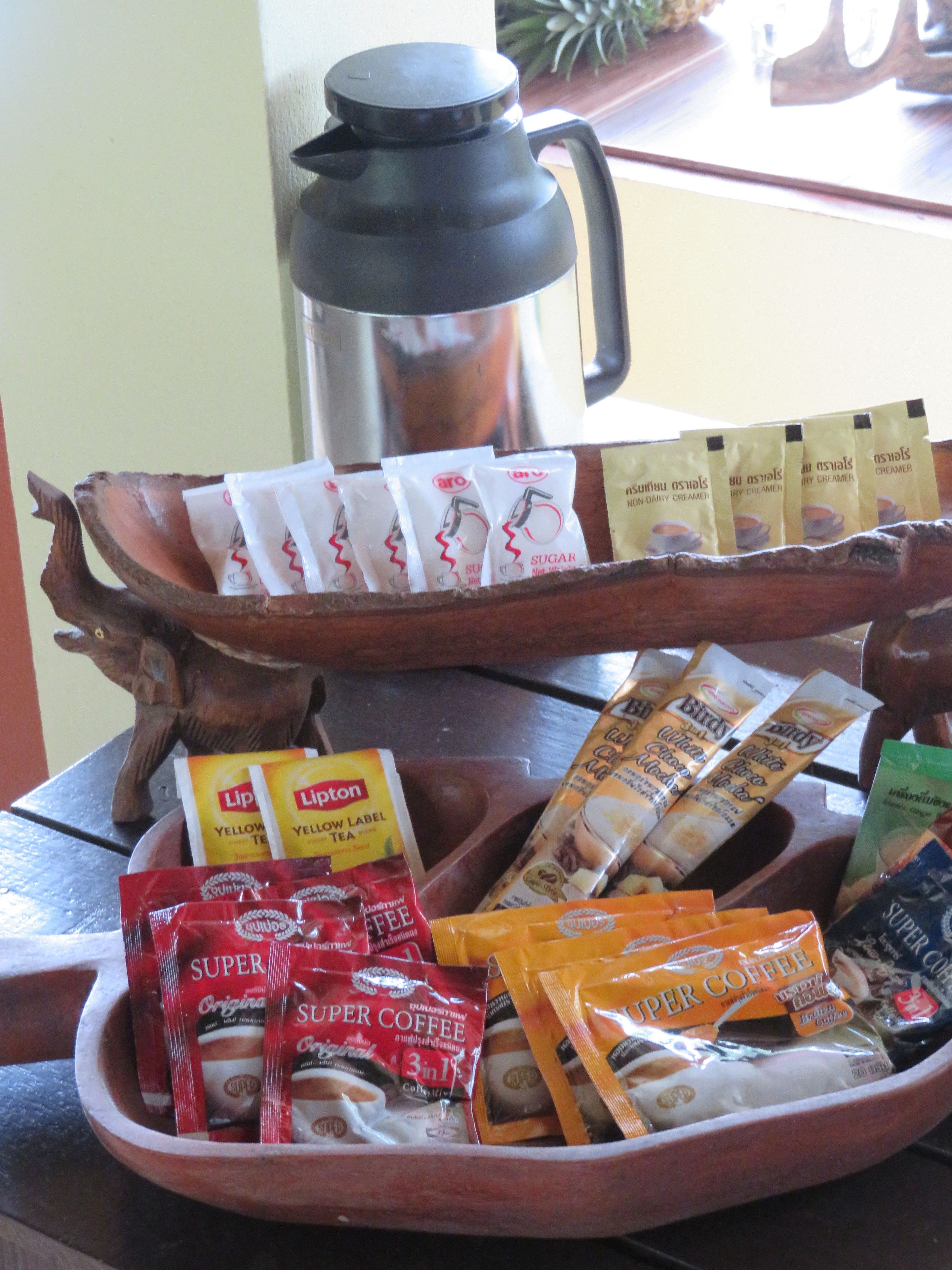 A tray with various coffee and tea packets, a coffee pot, and a decorative wooden spoon.