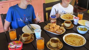 Dos niños sentados en una mesa con alimentos para el desayuno, como tortitas, magdalenas y jugo.