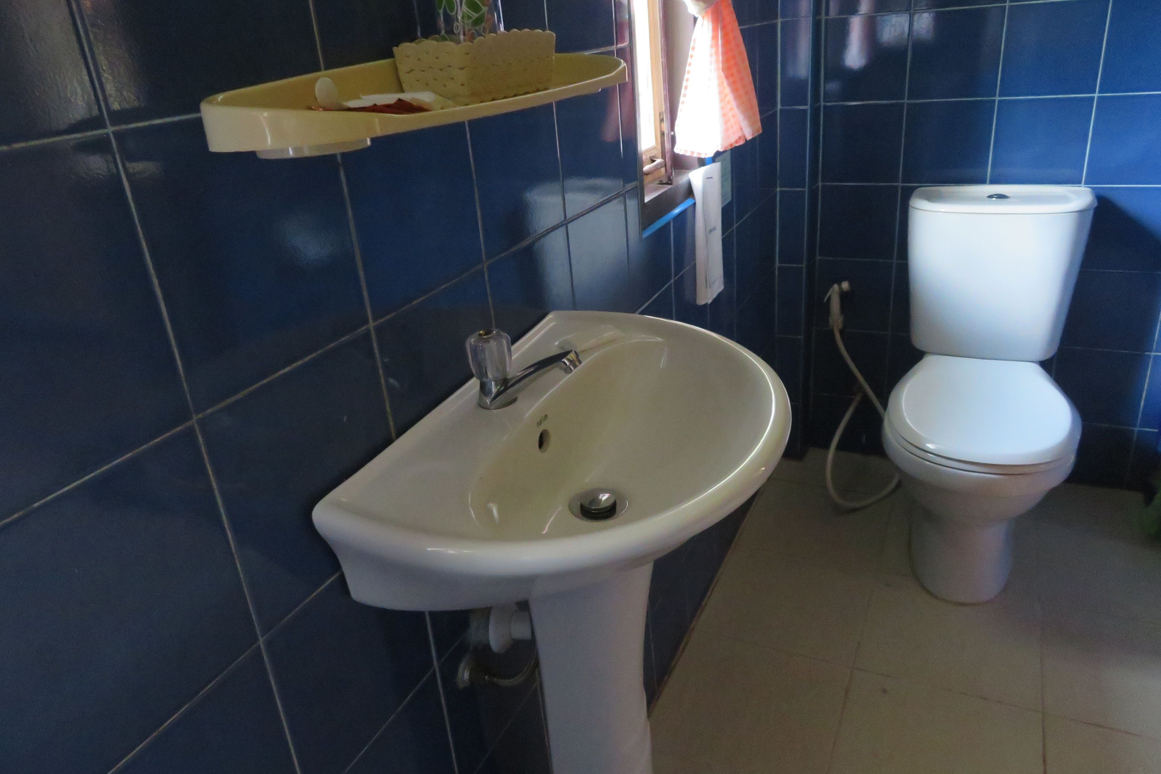 Un baño con lavamanos blanco, inodoro y estante sobre el lavamanos.