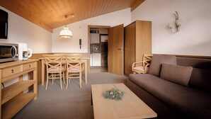 Espaço compacto para viver, com teto de madeira, cozinha compacta, área de refeições com mesa e cadeiras, sofá e pequena mesa de centro.