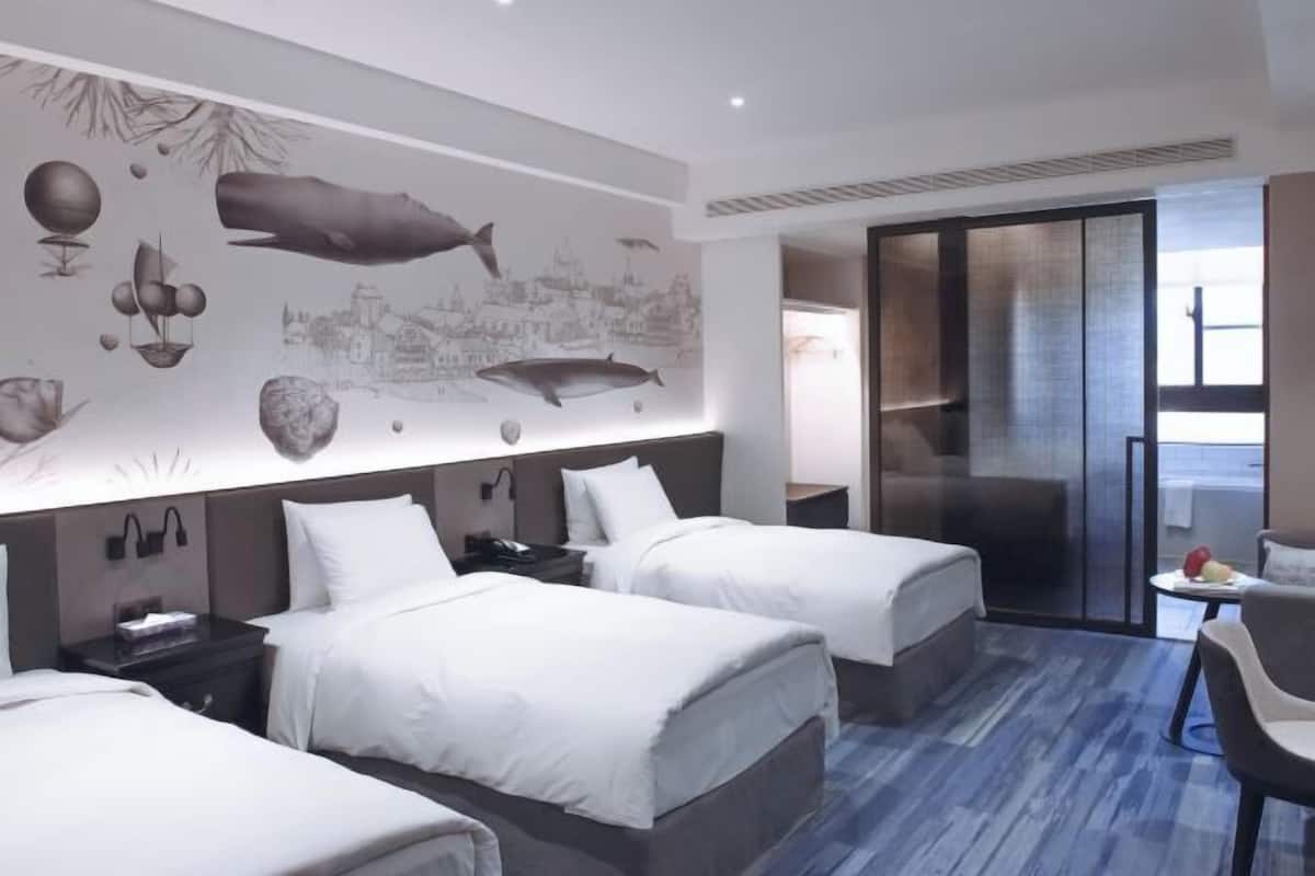 A hotel room with two beds, a large mural on the wall, a sliding door to a balcony, and a small table with fruit.