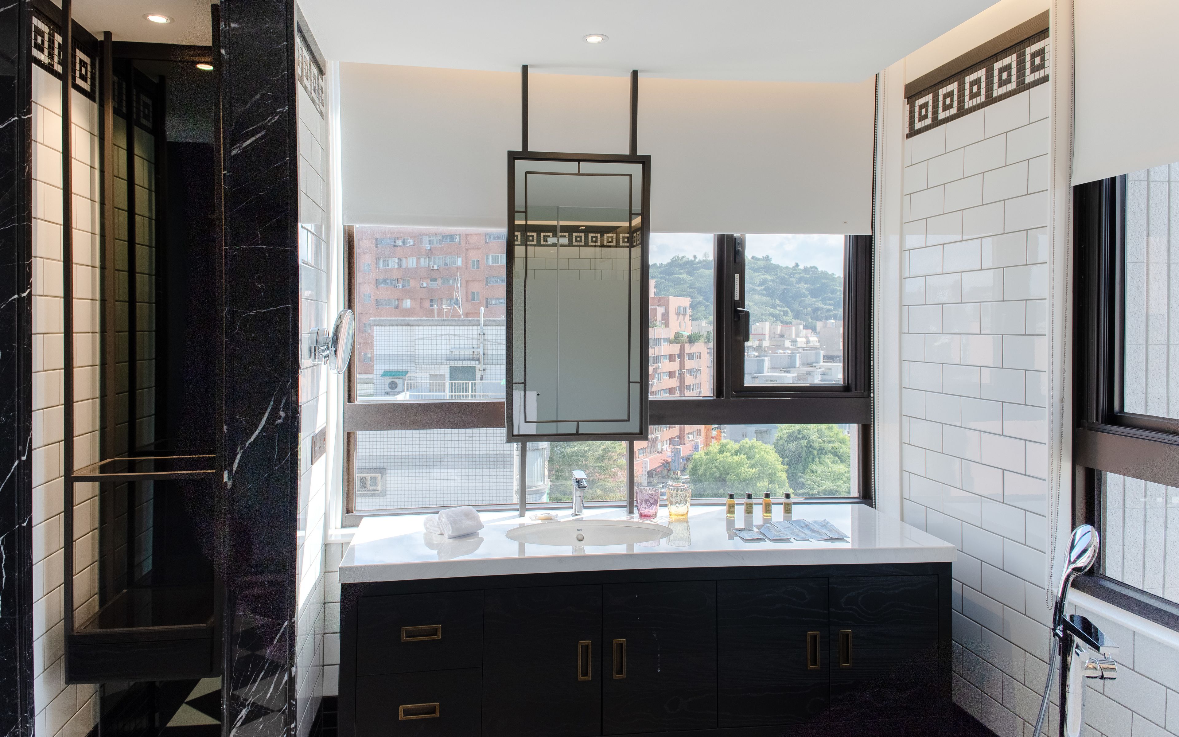A modern bathroom with a large mirror, a sink with toiletries, and a view of buildings through a window.